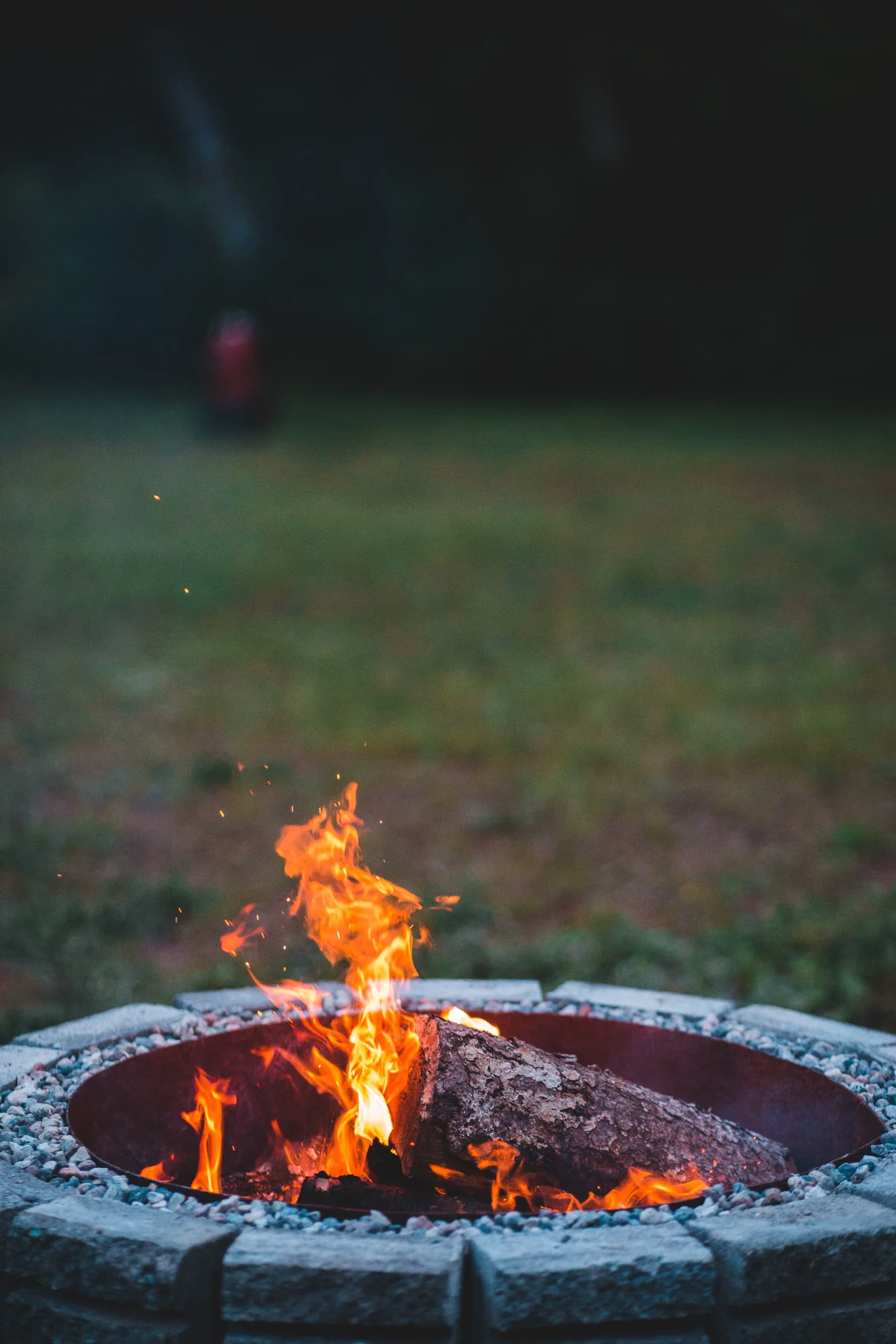Stone fire pit with flames at dusk beside a modern cabin patio